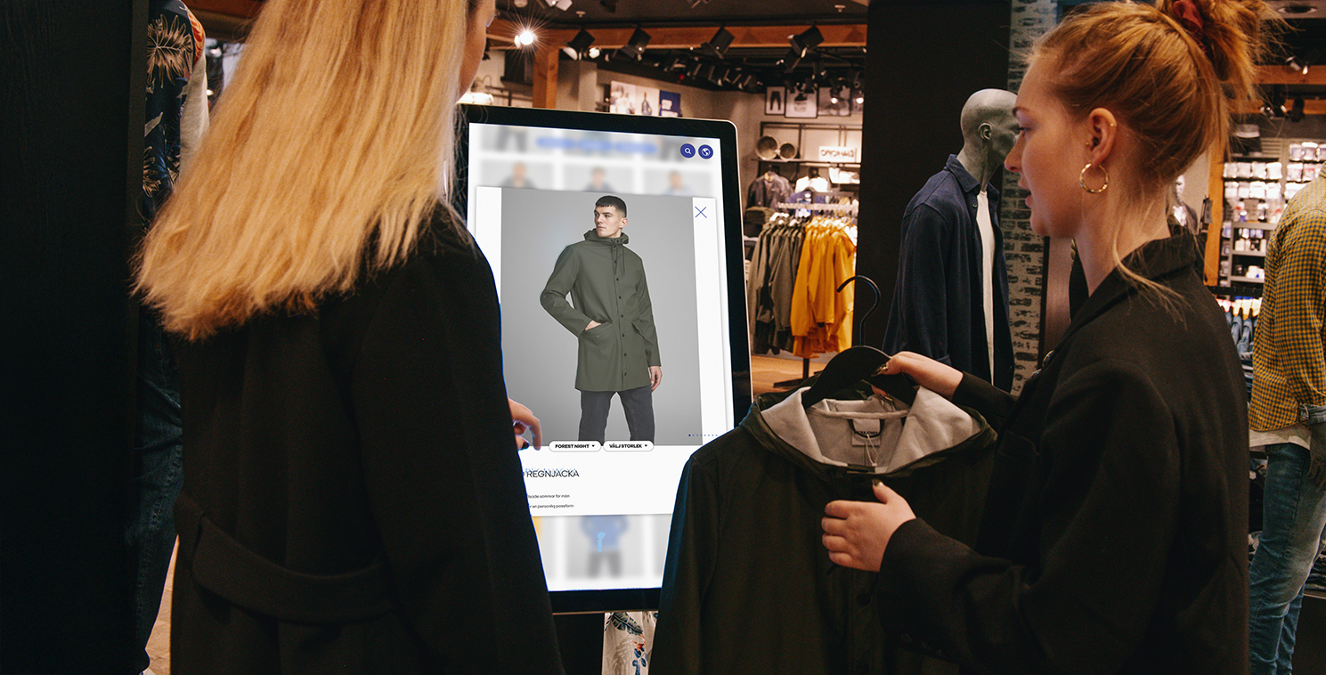 Deux clientes utilisent un grand écran tactile dans un magasin pour explorer des options de vêtements virtuels, illustrant la technologie immersive en magasin et l’engagement client personnalisé.