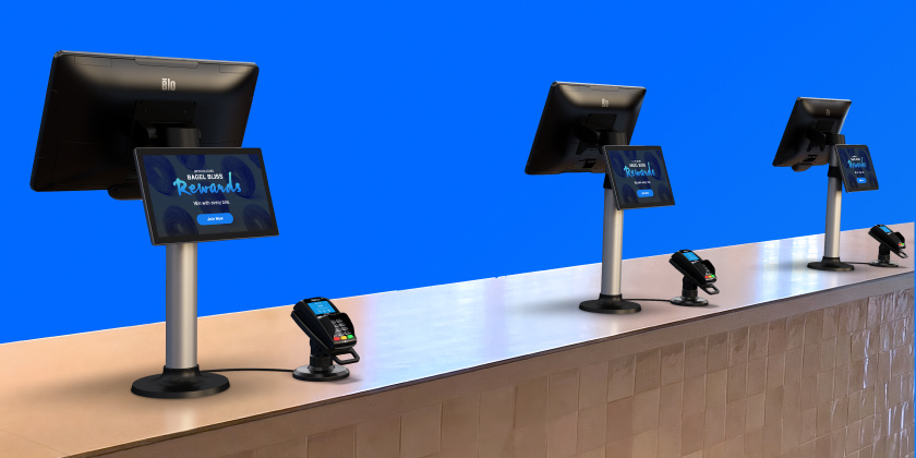 Plusieurs écrans tactiles Elo installés sur des supports le long d'un comptoir de caisse, chacun diffusant du contenu promotionnel numérique, avec des terminaux de paiement placés devant pour soutenir les supports publicitaires en magasin et les interactions au point de vente.